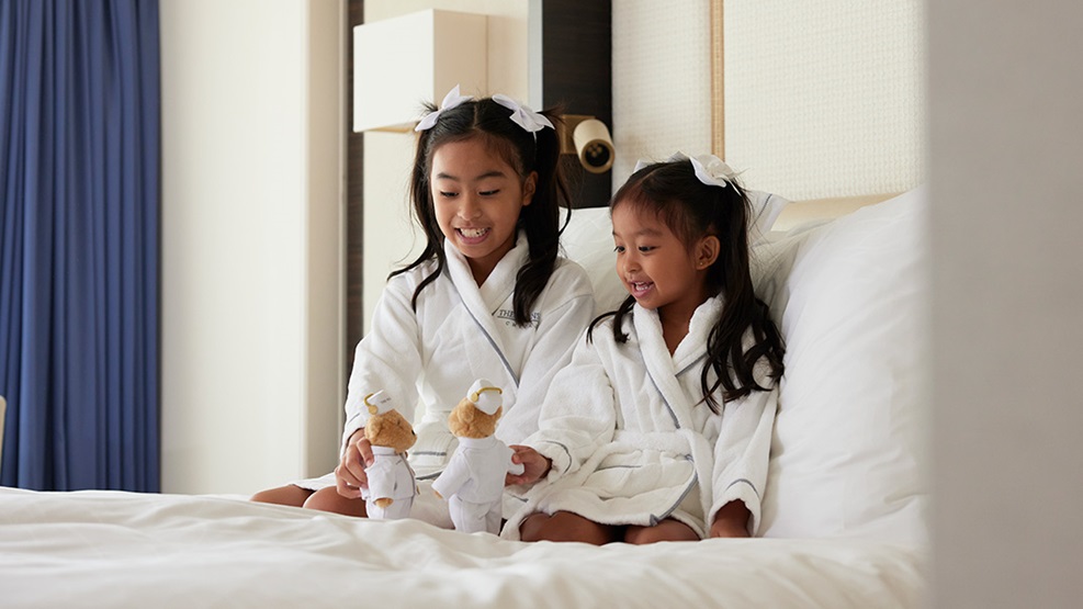 Two children sitting in hotel bed with stuffed animal bears